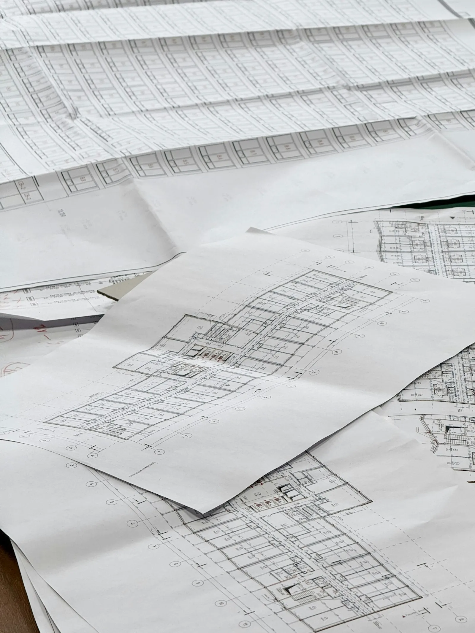 Tumpukan gambar denah dan blueprint konstruksi di atas meja kerja